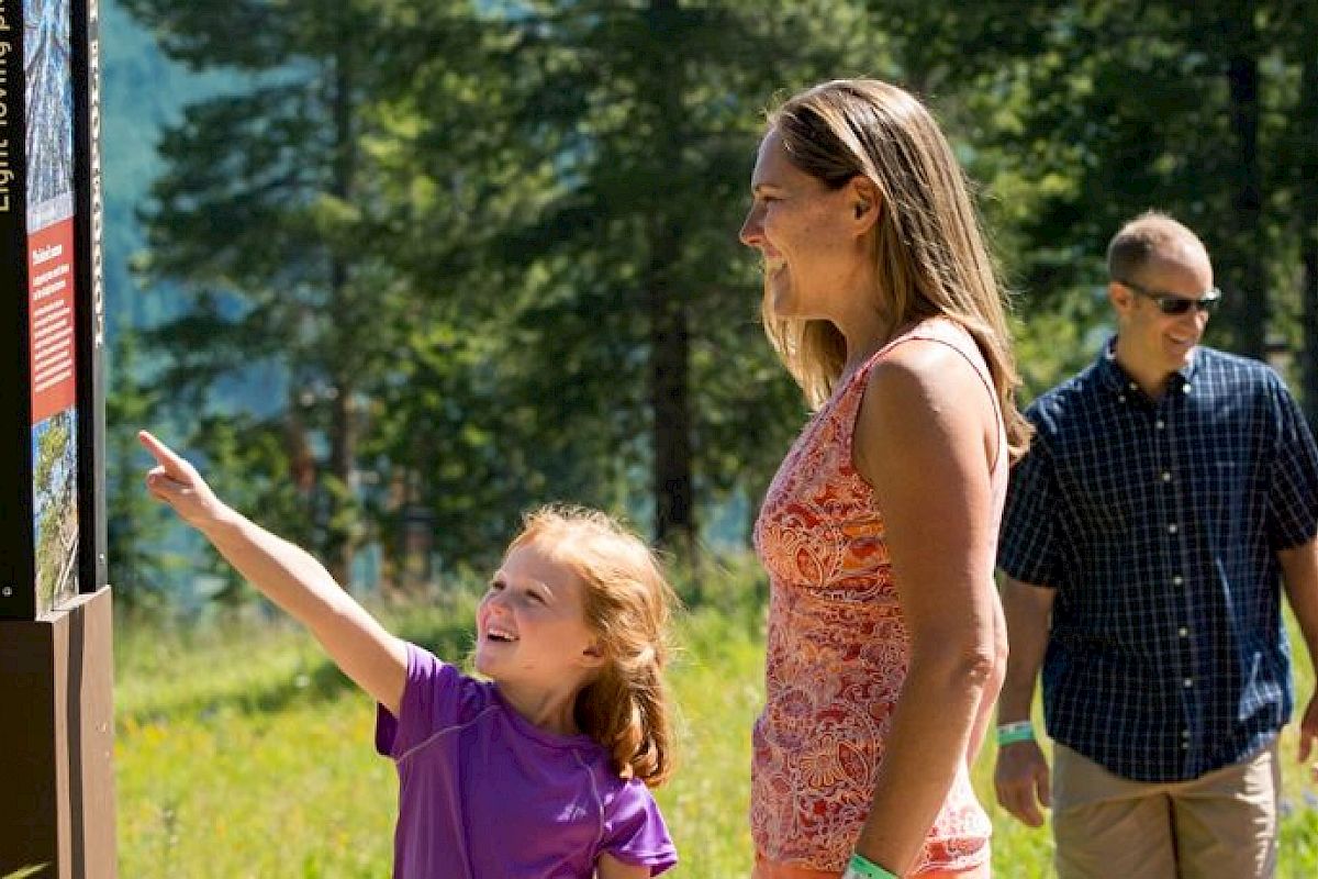 A family is enjoying a hike in a scenic forest area, reading information from a sign. They seem engaged and happy while exploring nature.