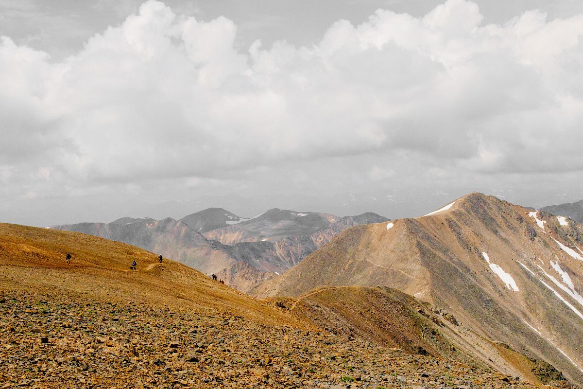 A mountainous landscape with rugged terrain and scattered patches of snow under a cloudy sky.