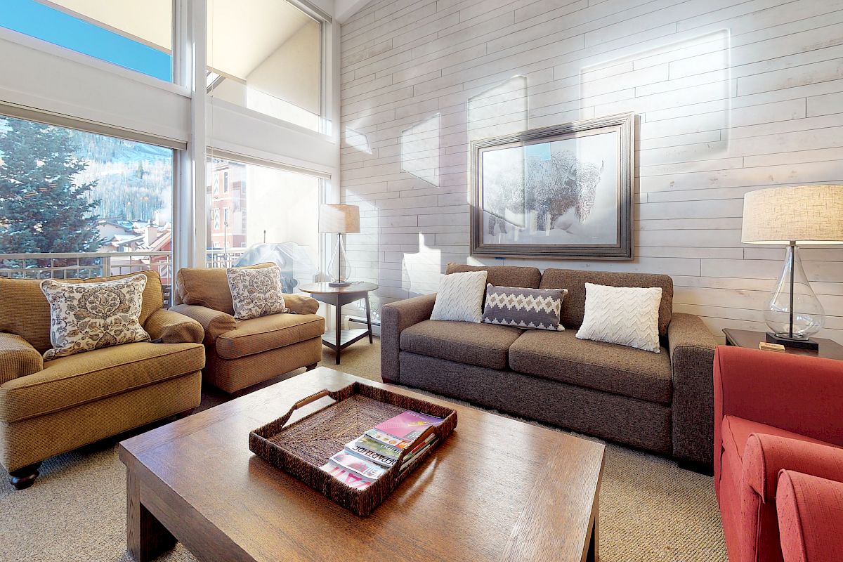 A cozy living room with a large window displaying a scenic view, featuring a brown sofa, two armchairs, a coffee table, and a framed picture ending the sentence.