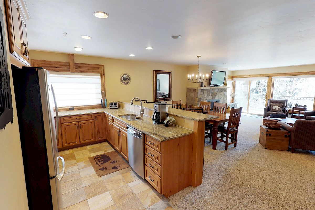 This is a spacious, open-concept kitchen and living area with modern appliances, wooden cabinetry, a dining table, and a cozy seating area with a fireplace.