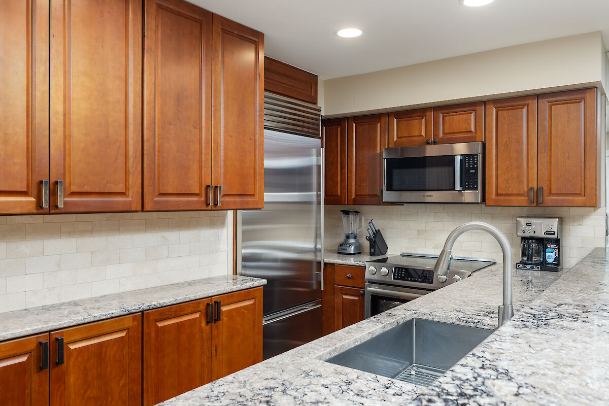 The image shows a modern kitchen with wooden cabinets, stainless steel appliances, and a granite countertop. It looks well-designed.