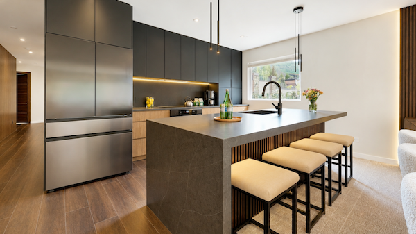 A modern kitchen with dark cabinets, a large island, bar stools, and stainless steel appliances; warm lighting and a clean, open vibe.