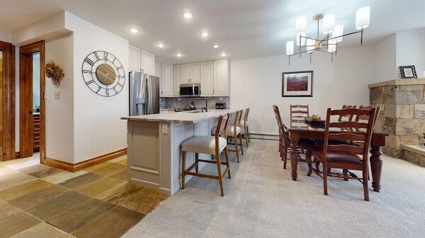 A modern kitchen and dining area with wooden chairs, a clock on the wall, and a chandelier hanging from the ceiling.